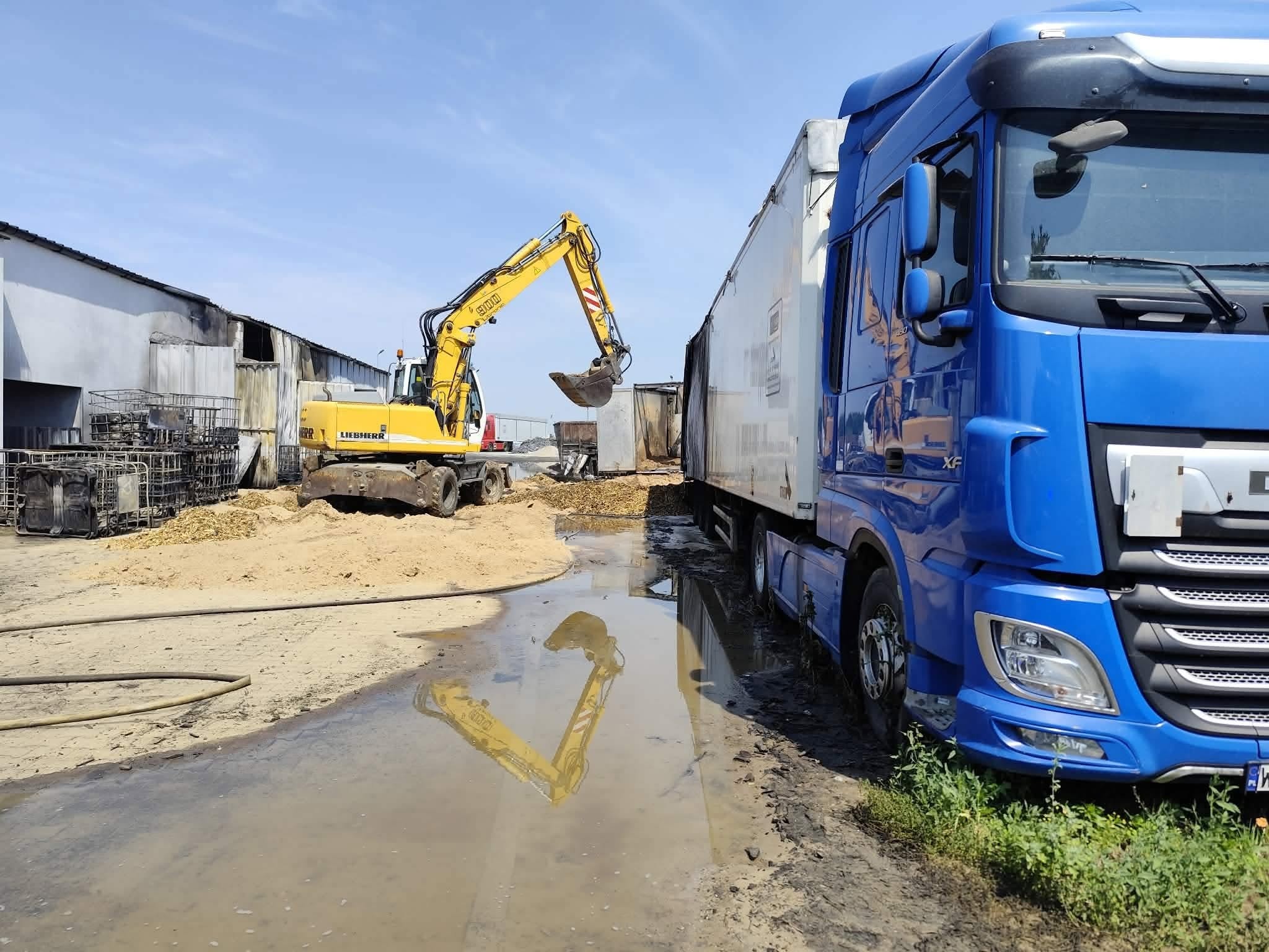 Koparka i samochód ciężarowy na terenie składowiska odpadów po pożarze w Mszczonowie